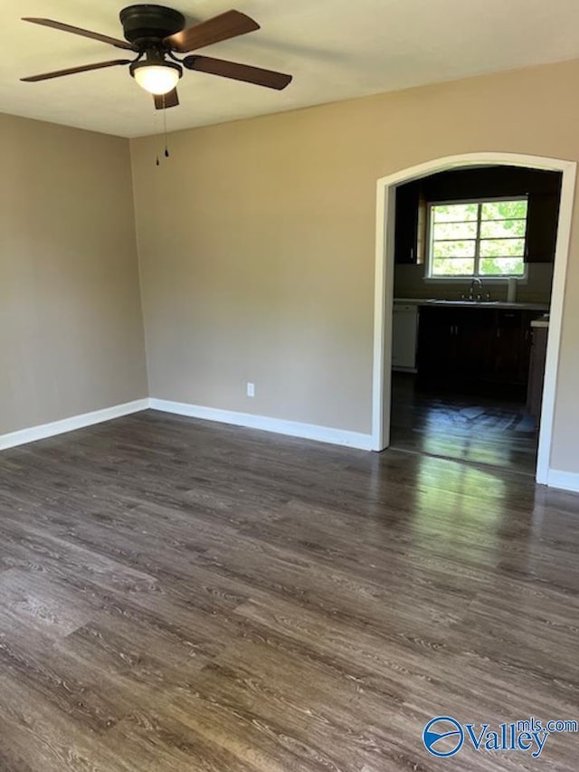 spare room featuring dark wood-style flooring, a ceiling fan, and baseboards