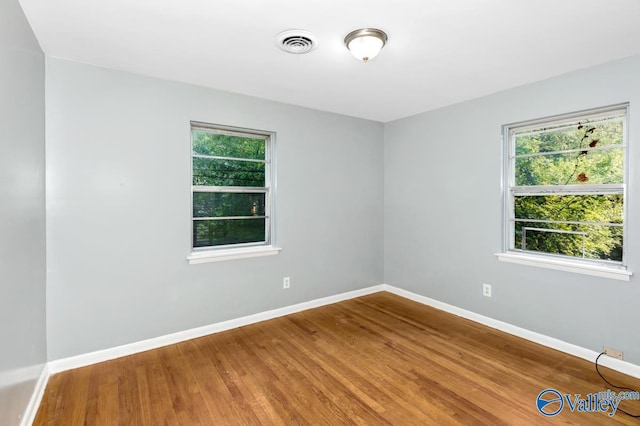 unfurnished room with wood finished floors, visible vents, and baseboards