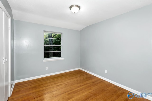 empty room with vaulted ceiling, wood finished floors, and baseboards