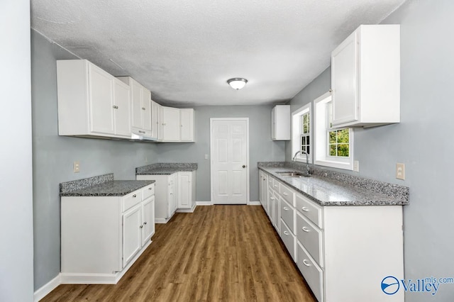 kitchen featuring stone countertops, white cabinetry, a sink, wood finished floors, and baseboards