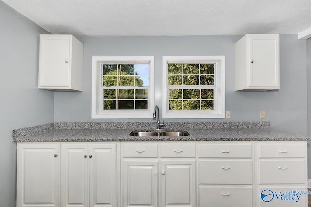 kitchen with stone counters, a textured ceiling, white cabinets, and a sink