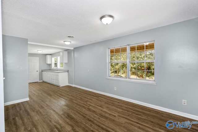 unfurnished living room featuring visible vents, baseboards, dark wood-style floors, a textured ceiling, and a sink