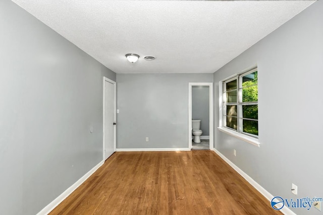 spare room with visible vents, baseboards, a textured ceiling, and wood finished floors