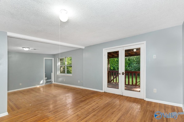 spare room featuring a textured ceiling, french doors, wood finished floors, and baseboards