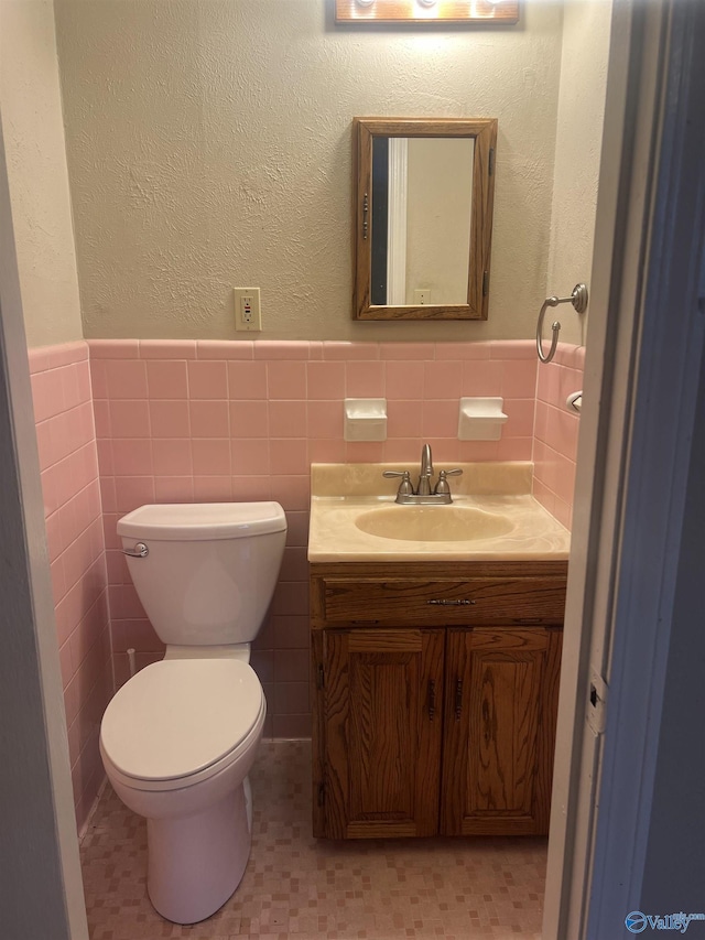 half bath featuring a wainscoted wall, toilet, vanity, and tile walls