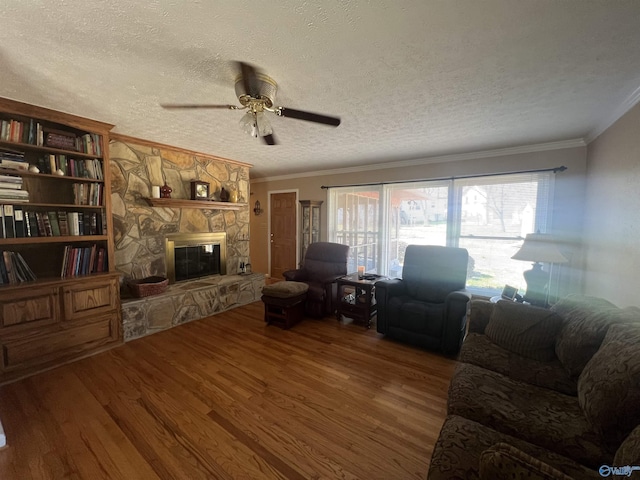 living room with a textured ceiling, wood finished floors, a stone fireplace, crown molding, and ceiling fan