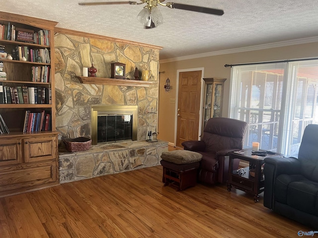 living room featuring wood finished floors, a fireplace, ceiling fan, a textured ceiling, and crown molding