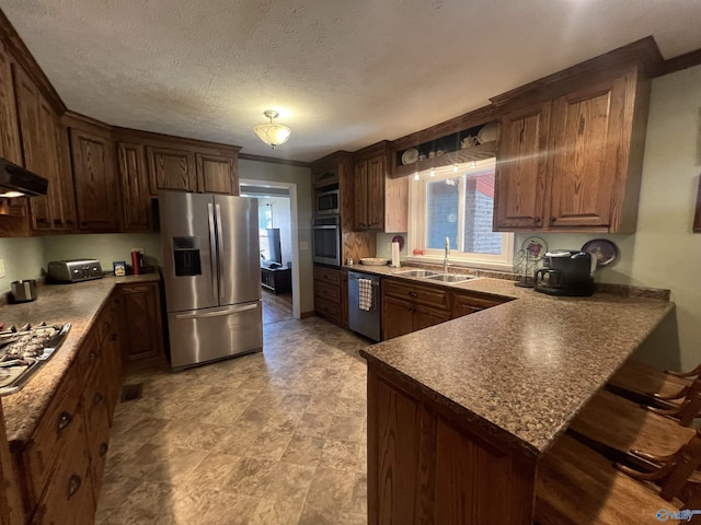 kitchen featuring a sink, a kitchen breakfast bar, a textured ceiling, appliances with stainless steel finishes, and a peninsula