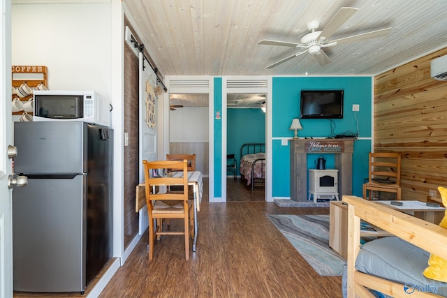 living room with dark wood-type flooring, ceiling fan, wooden ceiling, a barn door, and wood walls