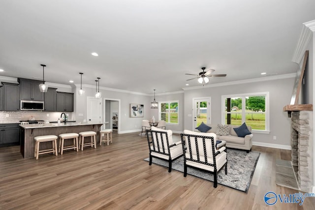 living room featuring sink, ornamental molding, ceiling fan, a stone fireplace, and light wood-type flooring