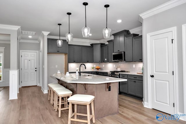 kitchen featuring stainless steel appliances, light hardwood / wood-style floors, a center island with sink, sink, and decorative light fixtures