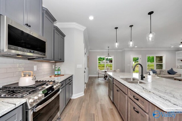 kitchen featuring stainless steel appliances, light stone counters, sink, a kitchen island with sink, and light hardwood / wood-style flooring