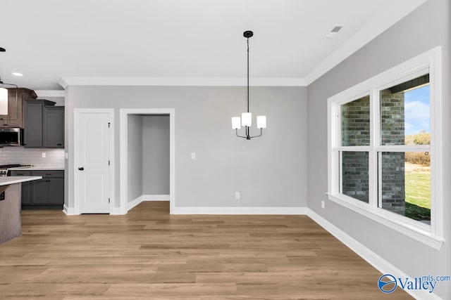 unfurnished dining area featuring ornamental molding, a notable chandelier, and light hardwood / wood-style floors