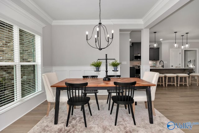 dining area featuring wood-type flooring, sink, crown molding, and an inviting chandelier