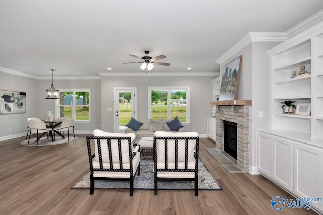 living room with a stone fireplace, light wood-type flooring, ceiling fan with notable chandelier, and crown molding