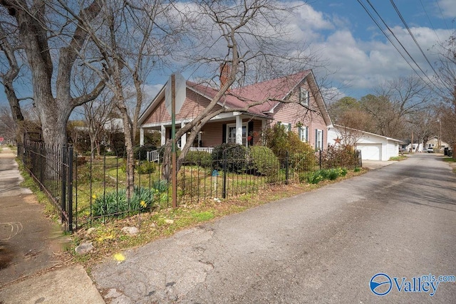 view of side of property with a fenced front yard, a detached garage, a porch, and a chimney