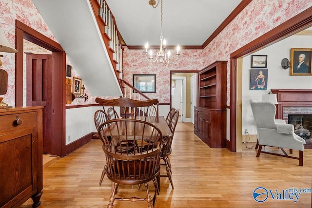 dining room featuring a high end fireplace, wallpapered walls, crown molding, a chandelier, and light wood-style flooring