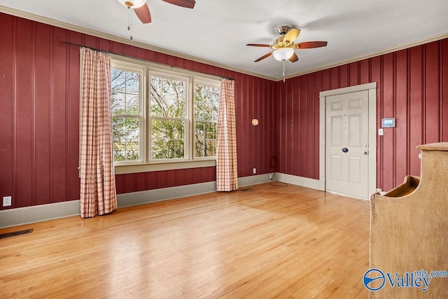 spare room featuring visible vents, ornamental molding, wood finished floors, baseboards, and ceiling fan