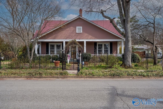 bungalow-style house featuring a fenced front yard, a porch, a chimney, and metal roof