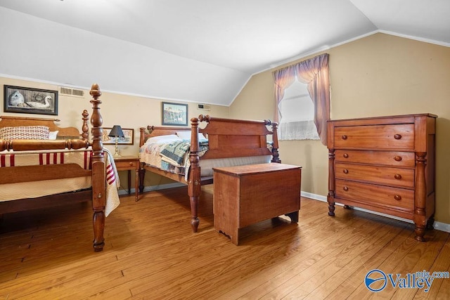 bedroom with vaulted ceiling, wood finished floors, visible vents, and baseboards