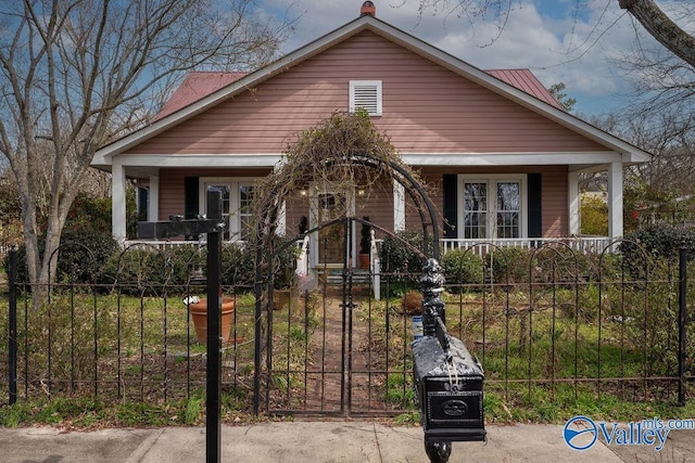 bungalow featuring a fenced front yard, covered porch, metal roof, and a gate