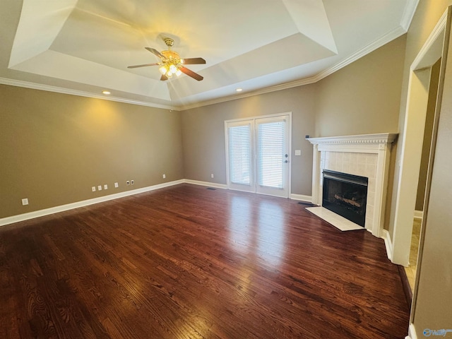 unfurnished living room with a ceiling fan, a raised ceiling, dark wood finished floors, and a tiled fireplace