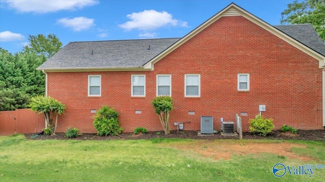 view of side of home featuring central AC unit, brick siding, a shingled roof, and a yard