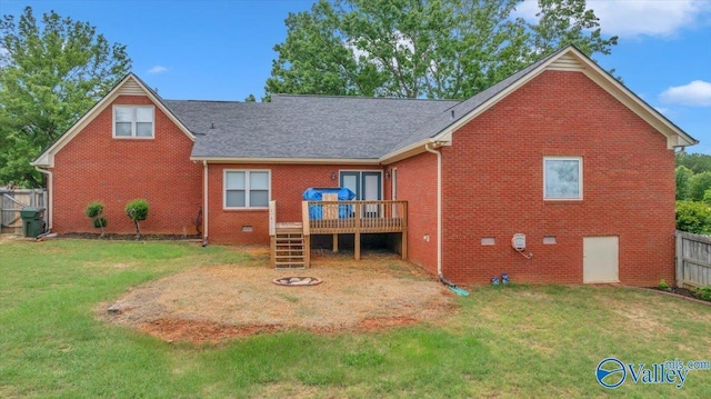 rear view of house with fence, a wooden deck, brick siding, and a lawn