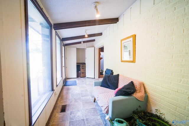 corridor with light tile patterned flooring, brick wall, a textured ceiling, and vaulted ceiling with beams