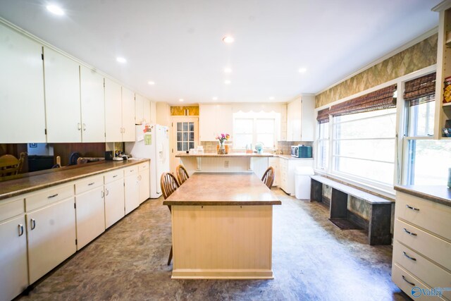 kitchen with a kitchen island, a breakfast bar area, white refrigerator with ice dispenser, and white cabinetry