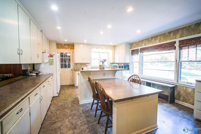 kitchen with white fridge, white cabinetry, a kitchen island, a kitchen breakfast bar, and backsplash