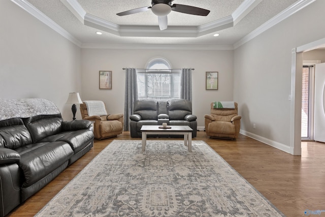 living area with baseboards, a raised ceiling, wood finished floors, crown molding, and a textured ceiling