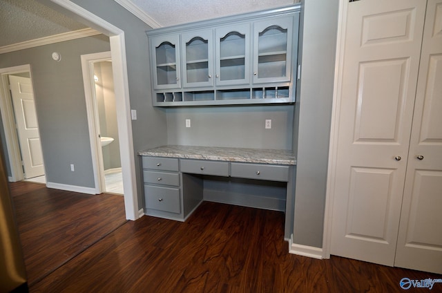 unfurnished office featuring built in desk, crown molding, dark wood-type flooring, and a textured ceiling