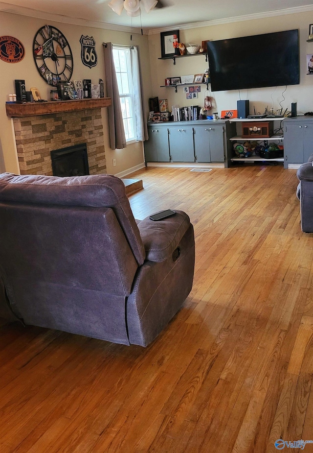 living room featuring ceiling fan, ornamental molding, a fireplace, and light hardwood / wood-style flooring