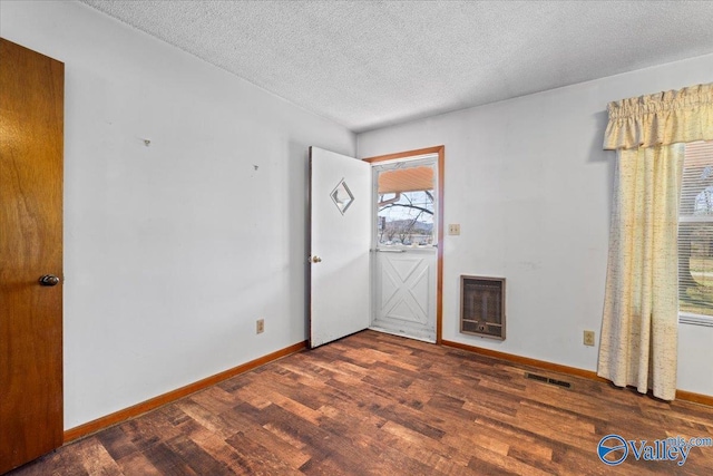 empty room featuring baseboards, visible vents, wood finished floors, heating unit, and a textured ceiling