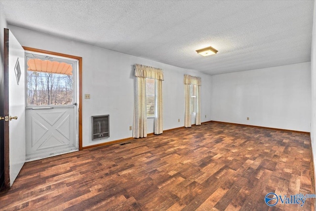 empty room with heating unit, a textured ceiling, baseboards, and wood finished floors