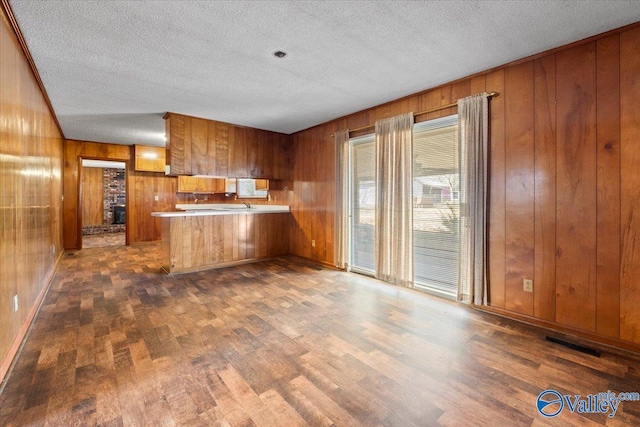 kitchen with visible vents, brown cabinetry, dark wood-style floors, a peninsula, and wood walls