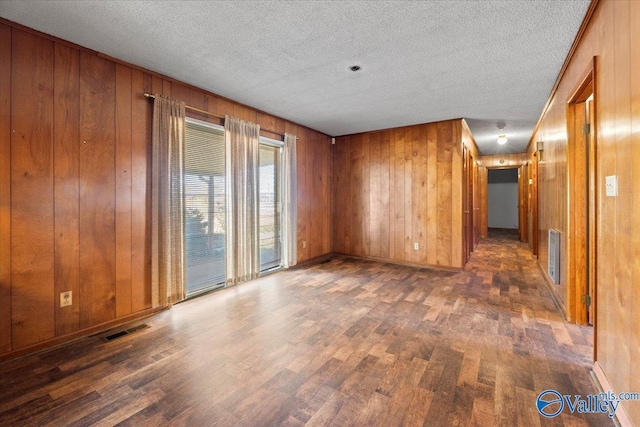 empty room with wooden walls, visible vents, and wood finished floors