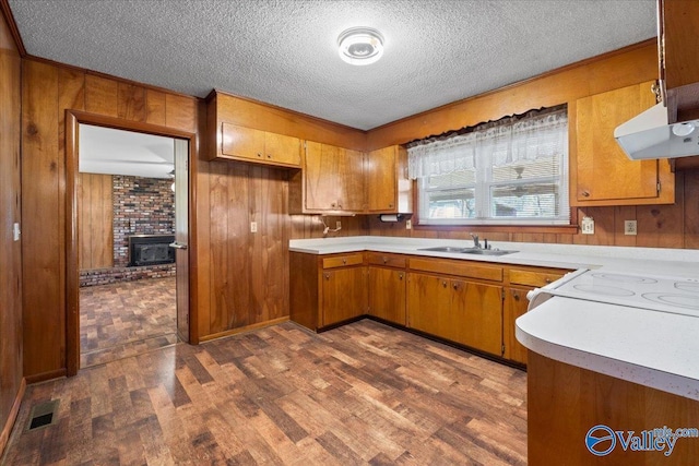 kitchen featuring wooden walls, brown cabinets, light countertops, and under cabinet range hood