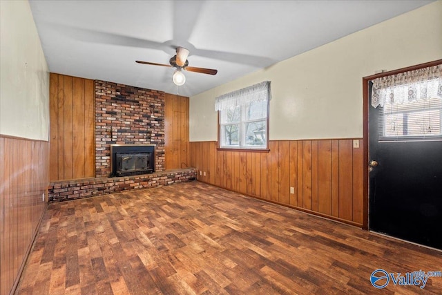 unfurnished living room with a ceiling fan, wainscoting, wooden walls, and wood finished floors