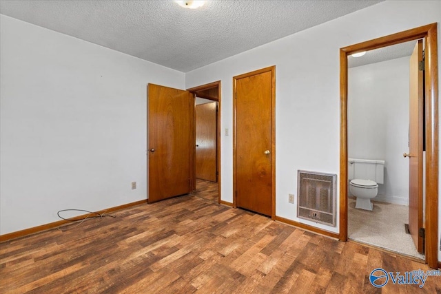 unfurnished bedroom featuring baseboards, a textured ceiling, wood finished floors, and heating unit