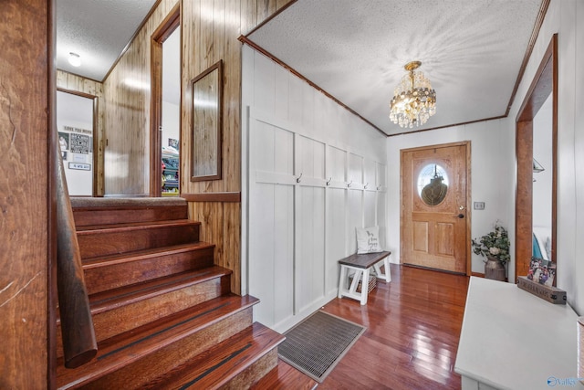 entryway with wood-type flooring, a chandelier, a textured ceiling, ornamental molding, and wooden walls