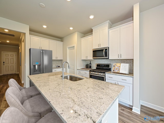 kitchen with stainless steel appliances, a sink, wood finished floors, a kitchen island with sink, and white cabinetry