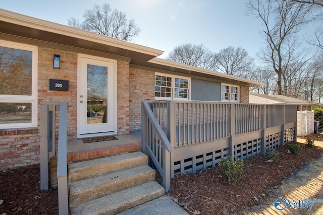 doorway to property featuring a garage, brick siding, and a deck