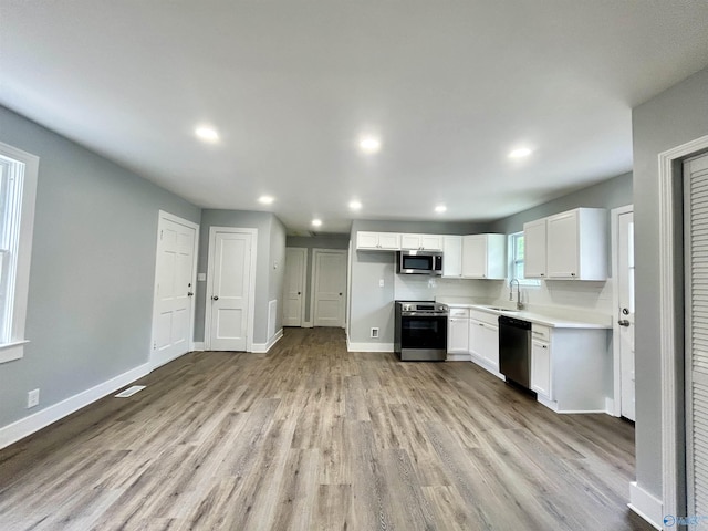 kitchen with baseboards, white cabinets, a sink, light wood-style flooring, and stainless steel appliances