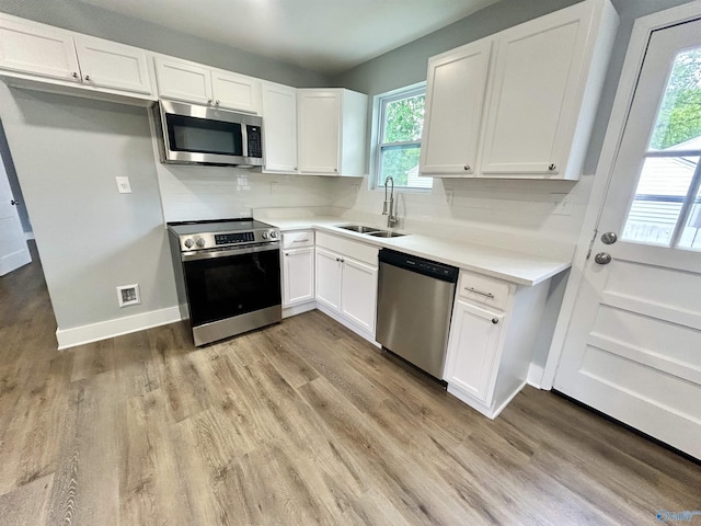 kitchen with appliances with stainless steel finishes, a sink, light wood finished floors, light countertops, and white cabinetry