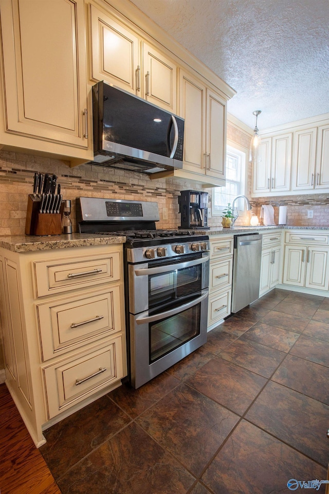 kitchen with decorative backsplash, stainless steel appliances, hanging light fixtures, and cream cabinetry