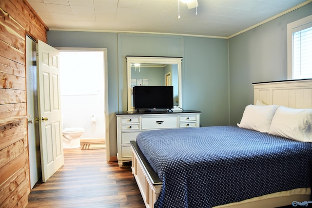 bedroom featuring ensuite bath, ceiling fan, wooden walls, crown molding, and wood-type flooring