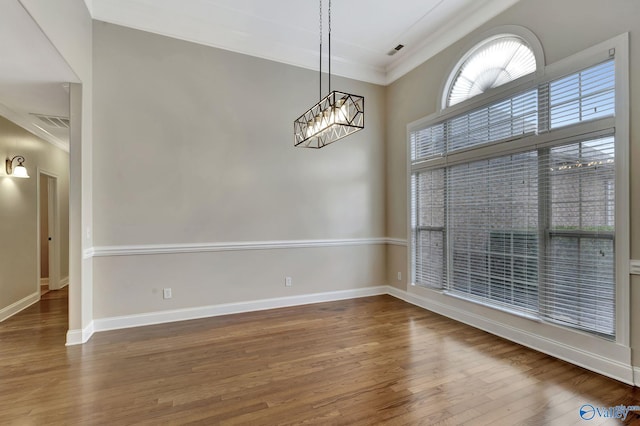 empty room featuring visible vents, an inviting chandelier, ornamental molding, wood finished floors, and baseboards