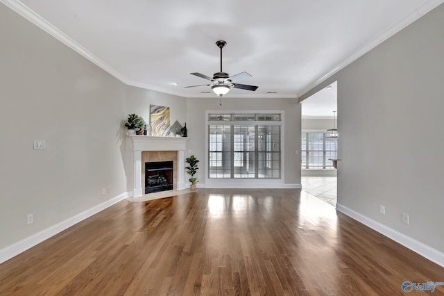 unfurnished living room featuring baseboards, ornamental molding, a tiled fireplace, and wood finished floors